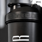 Close-up of the lid of the Warrior Home of Creatine Shaker 600ml in black, showing 'The Home of Creatine' embossed text and the Warrior logo on the body