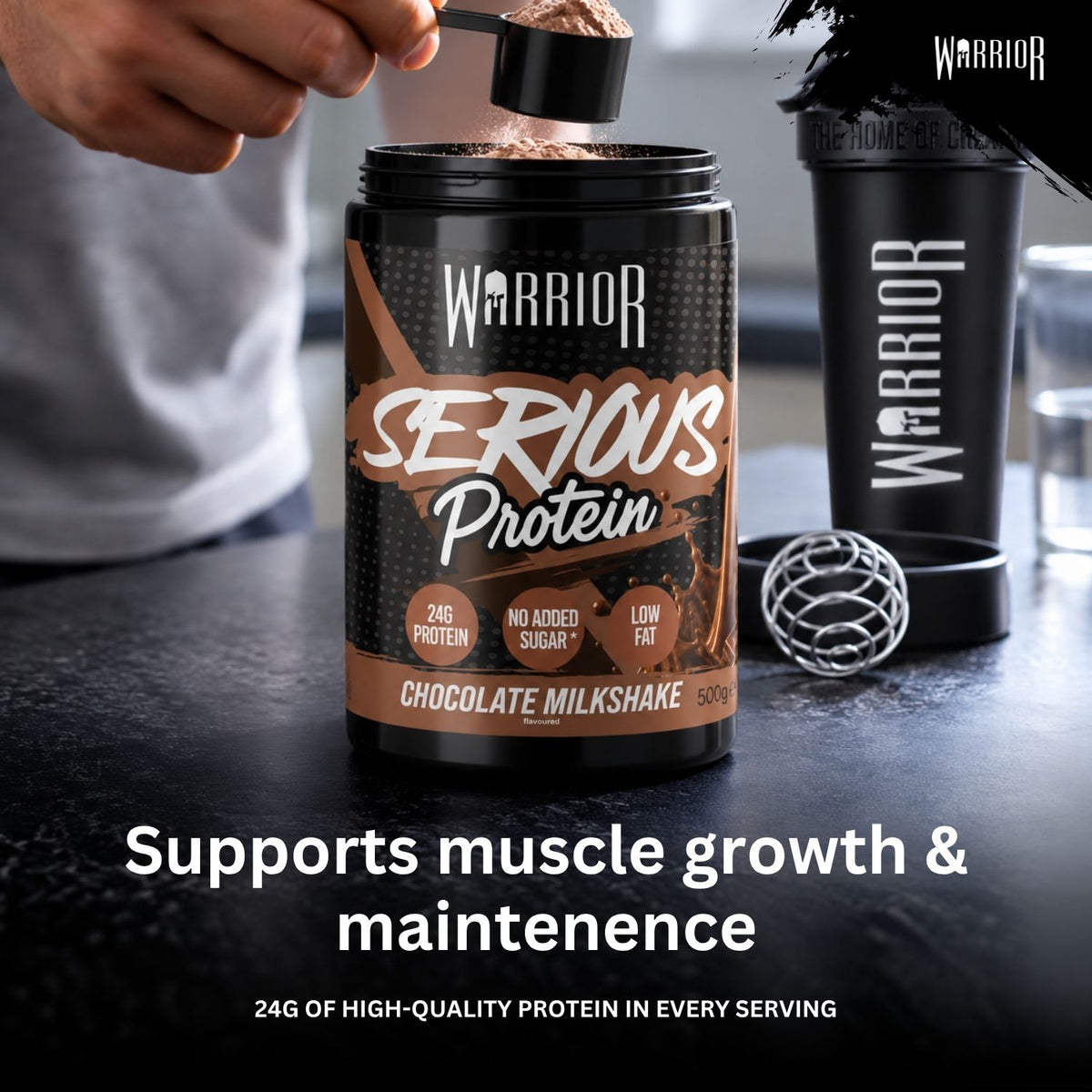 Warrior Serious Protein Chocolate Milkshake, 500g – hand adding a scoop of powder to the tub, with a matching shaker bottle and mixing ball on a dark countertop.
