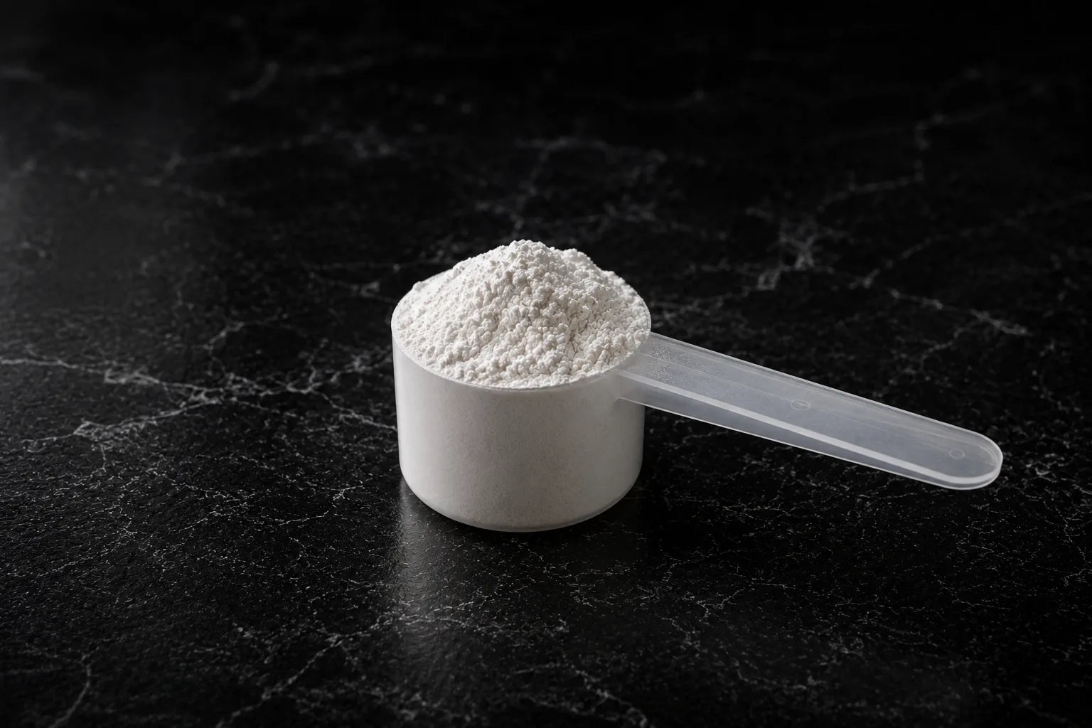 A scoop of creatine powder on dark marble